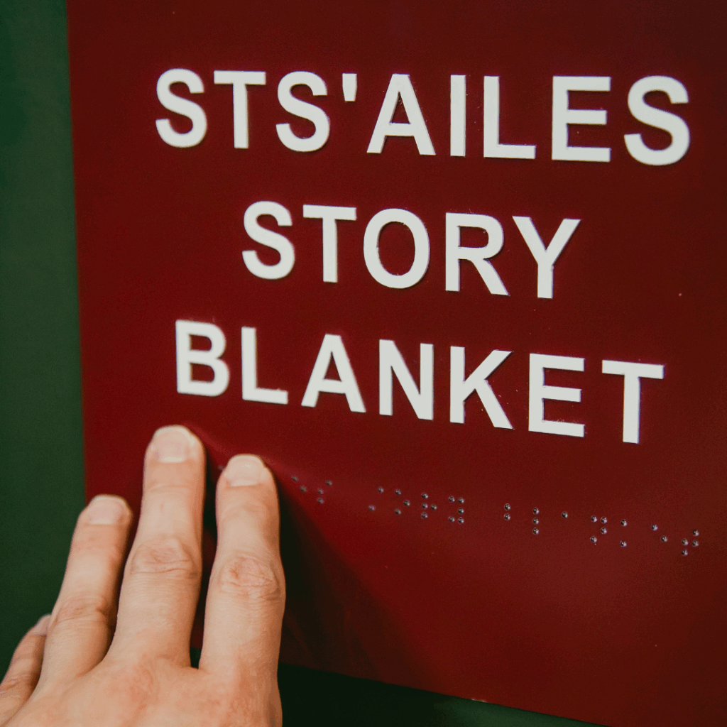 A hand reading braille for the words "Sts'ailes Story Blanket"
