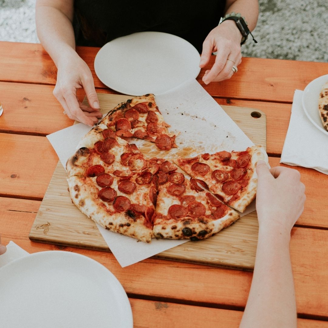 hands reaching for a pepperoni pizza