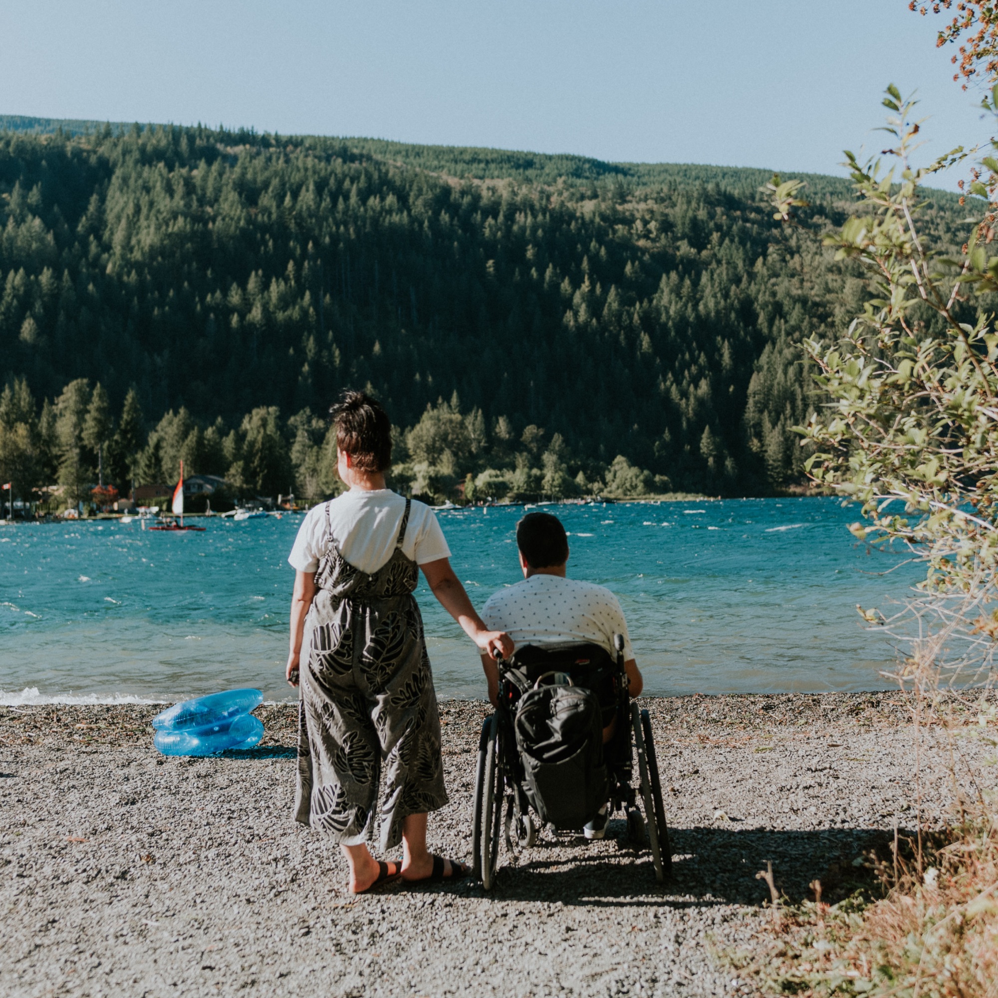 a woman and man in a wheelchair on a lake shore