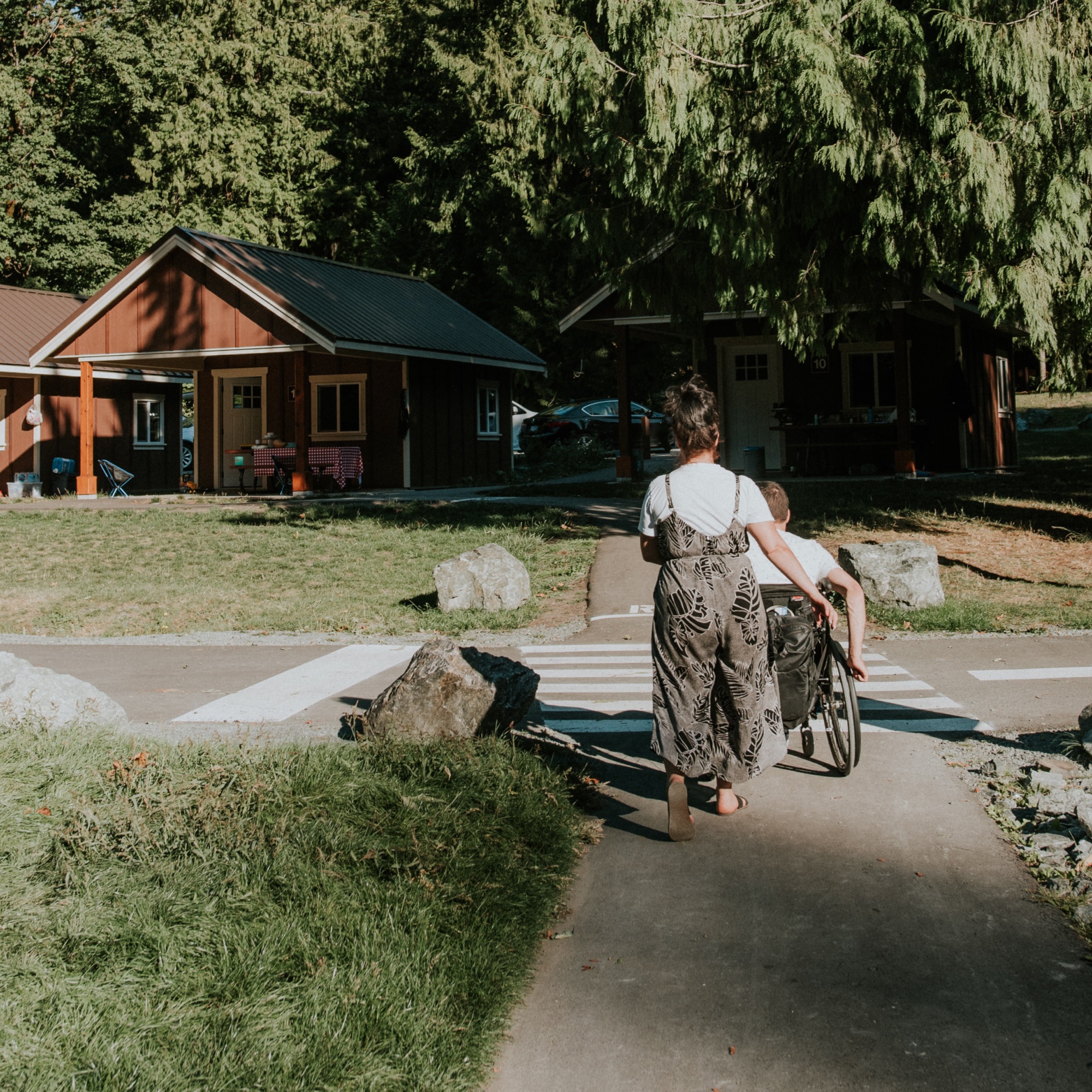 a woman and man in a wheelchair crossing a small road
