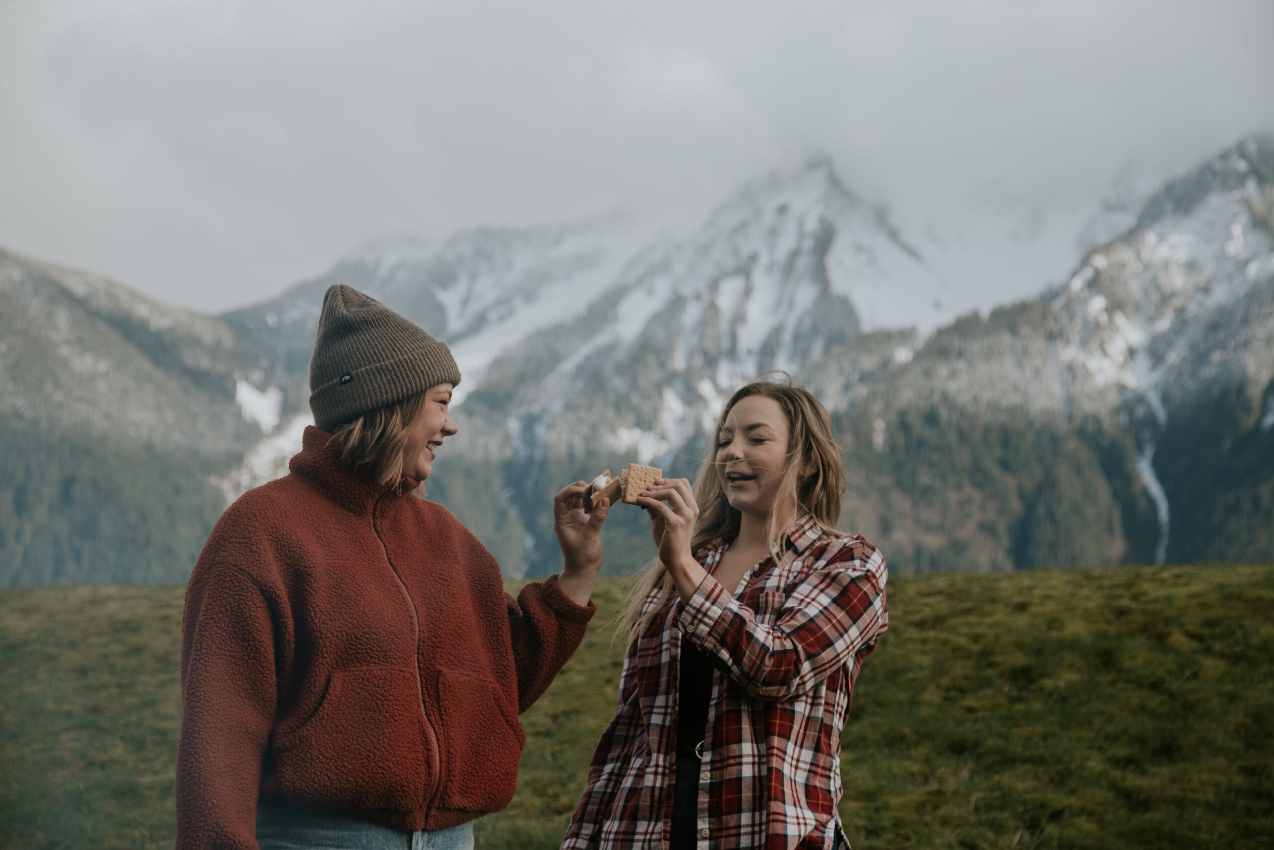 Two girls toasting their smores, with mountains in the background