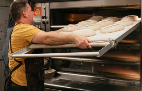 A man standing in a kitchen, putting in a tray of bread ready to be baked.