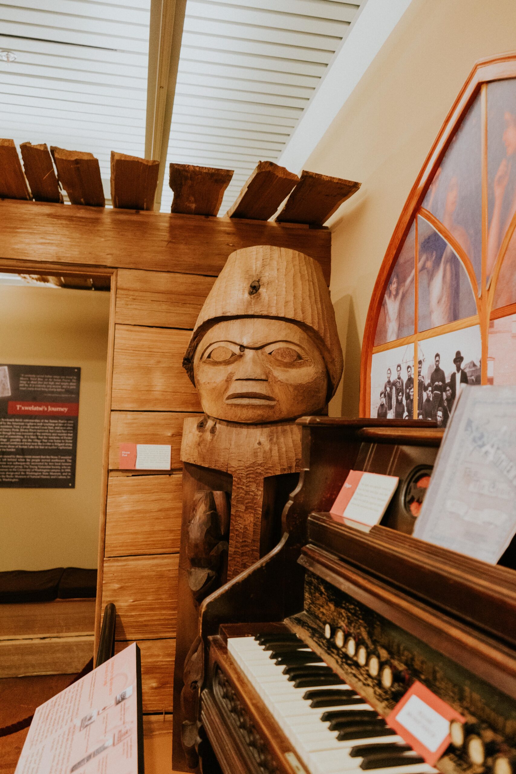 A wooden statue displayed in a museum, with a piano in the foreground.