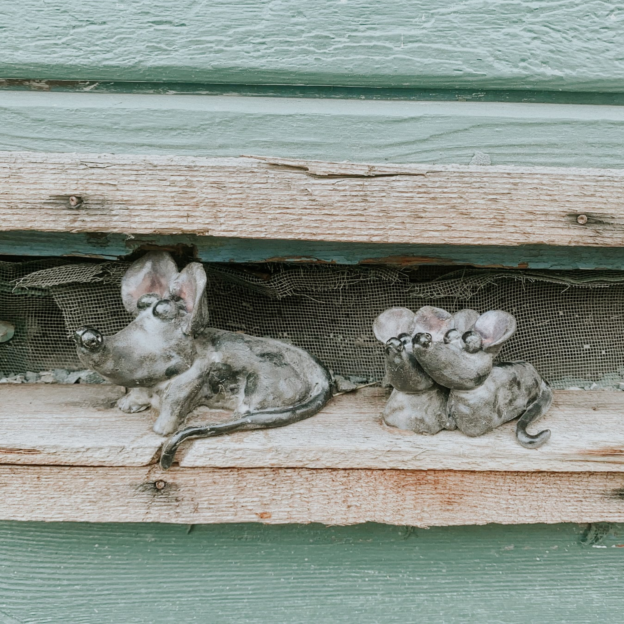 Wooden shelf with two wooden rats perched on it, one looking curiously at the camera, the other grooming itself calmly.