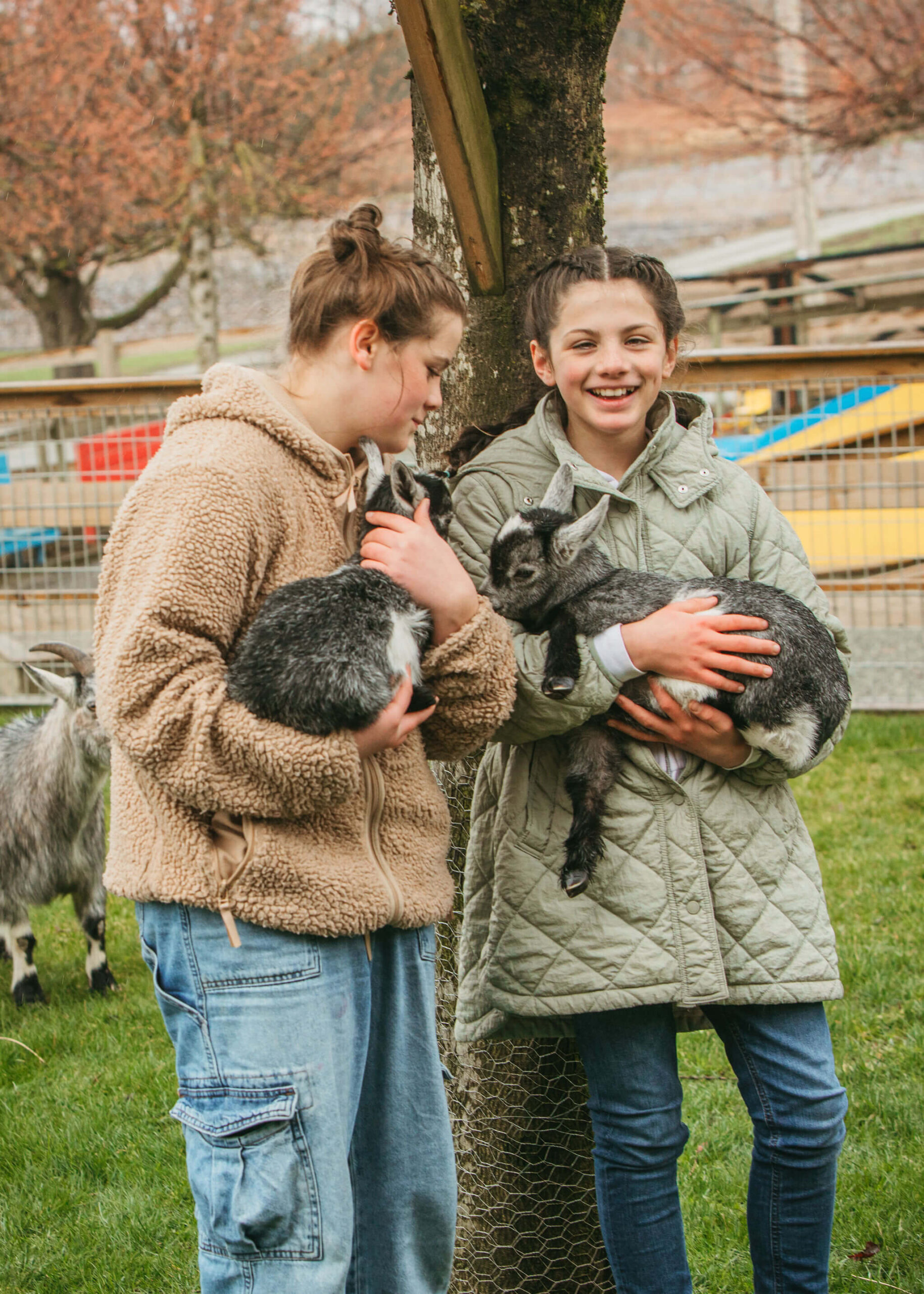 Two girls smiling as they hold a cute baby goat in their arms, enjoying a delightful moment together.