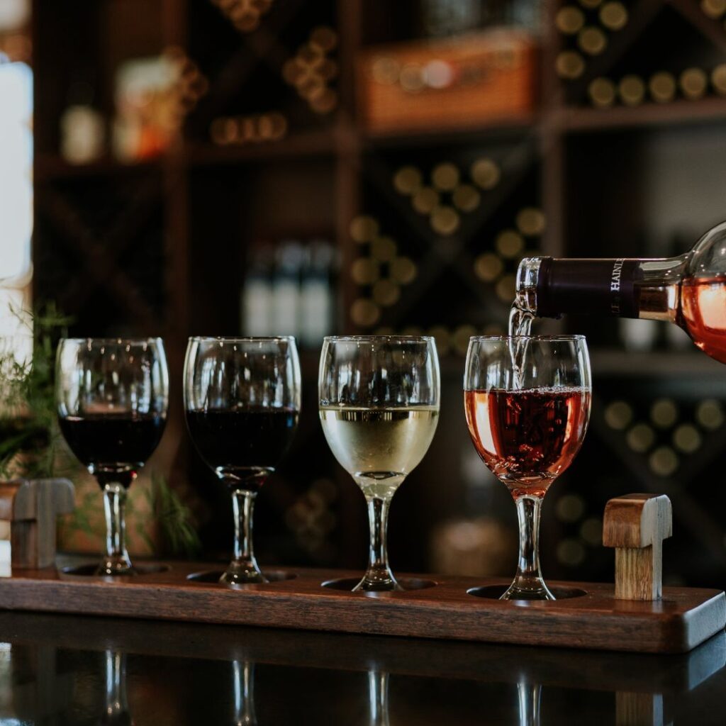 Wine is being poured into a glass, that sits on a wooden flight with other wine glasses.