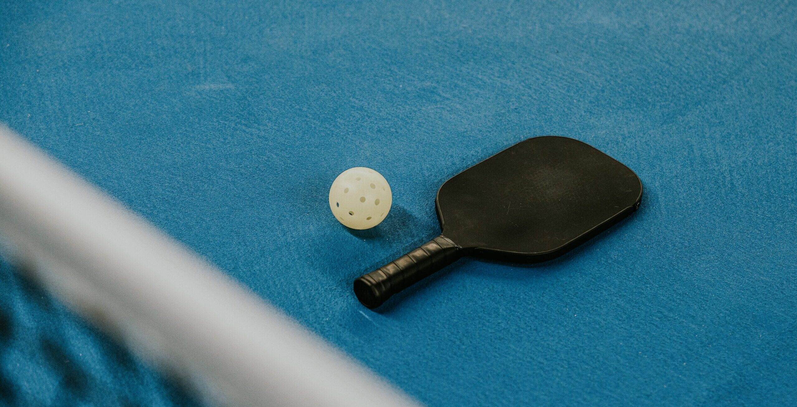 A pickleball racquet and ball on the floor of a court