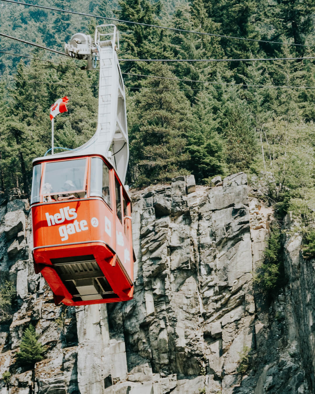 A bright red air tram hangs in the air next to a cliff face