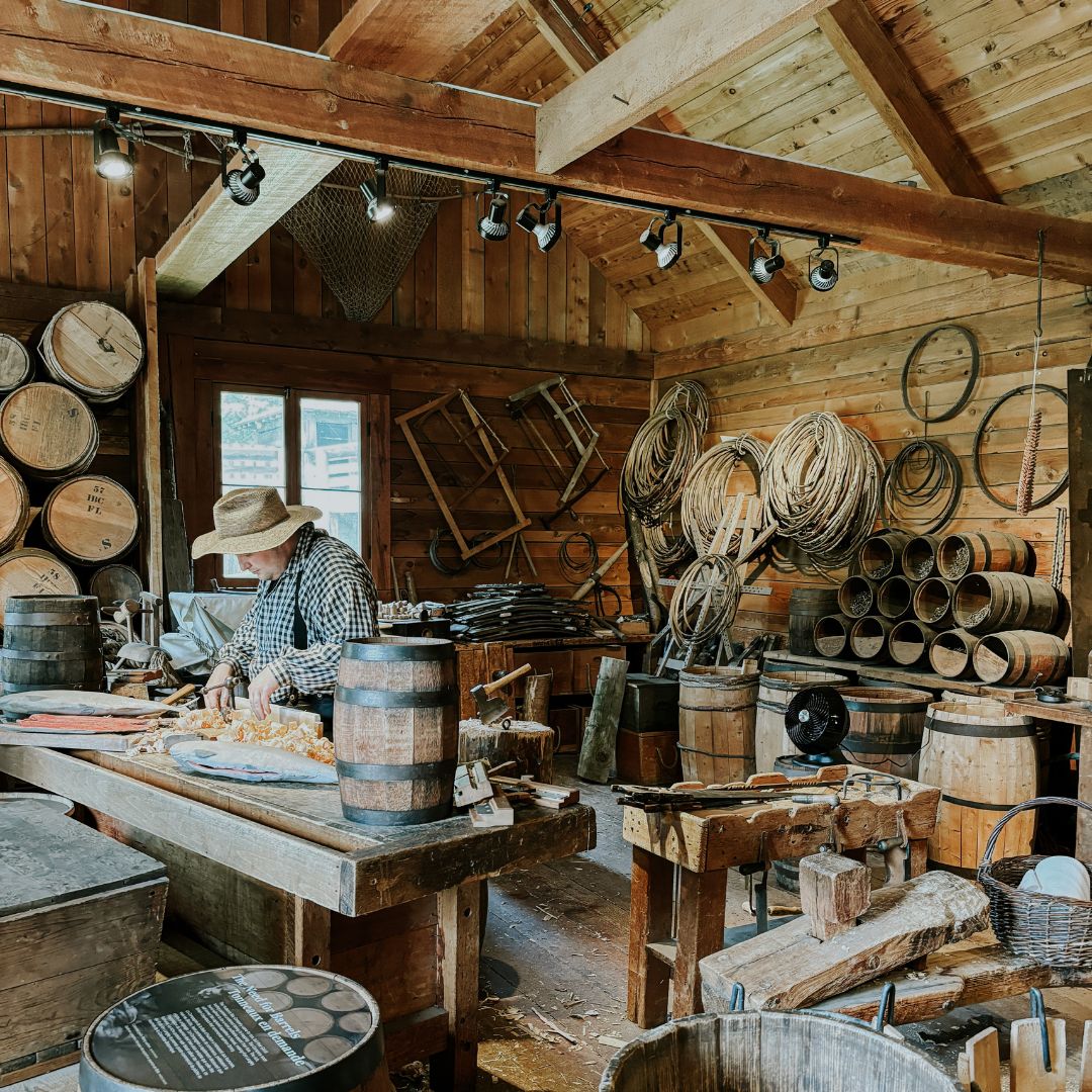 A man working in a woodworking shop surrounded by barrels and tools.
