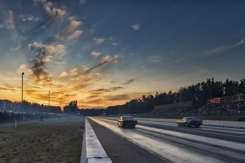 two cars racing down a raceway track at sunset