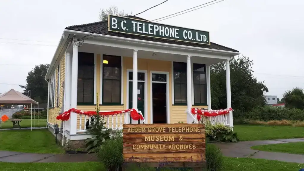 The outside of the Alder Grove Heritage Society & Telephone Museum, a small yellow house with a front porch.