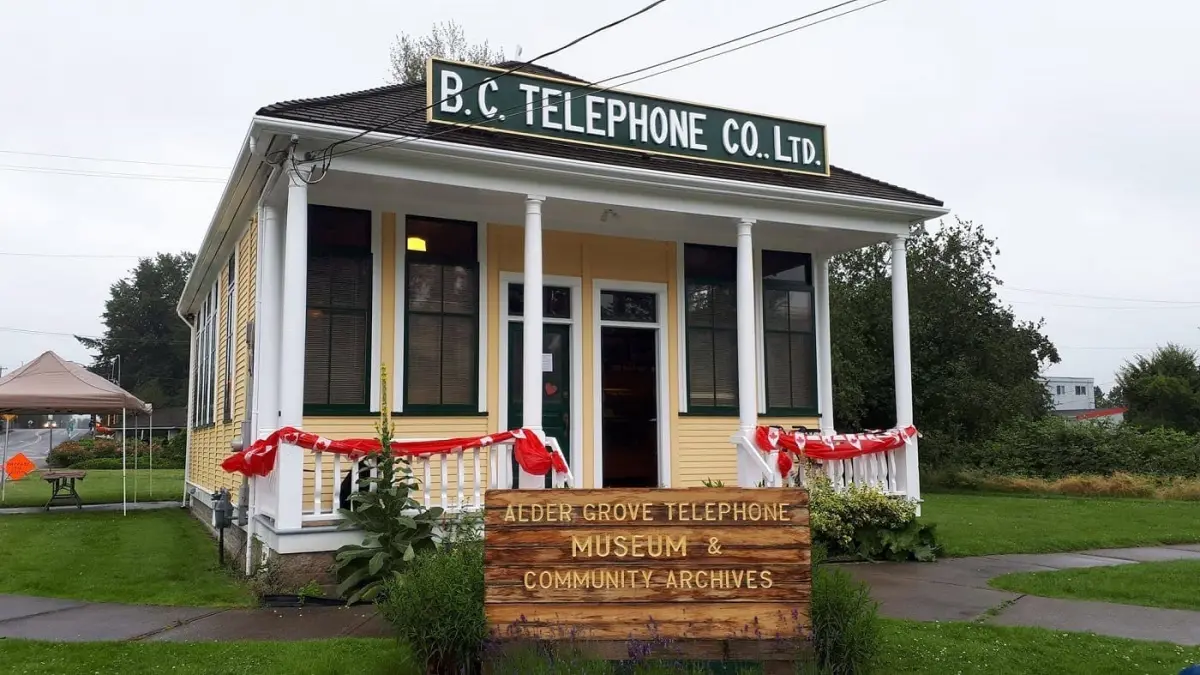 The outside of the Alder Grove Heritage Society & Telephone Museum, a small yellow house with a front porch.
