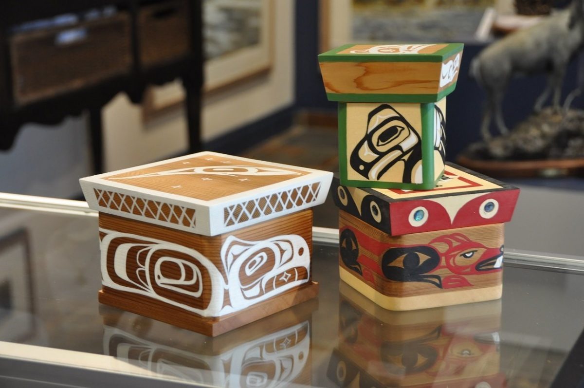 Three wooden boxes with Indigenous designs sit on a glass table.