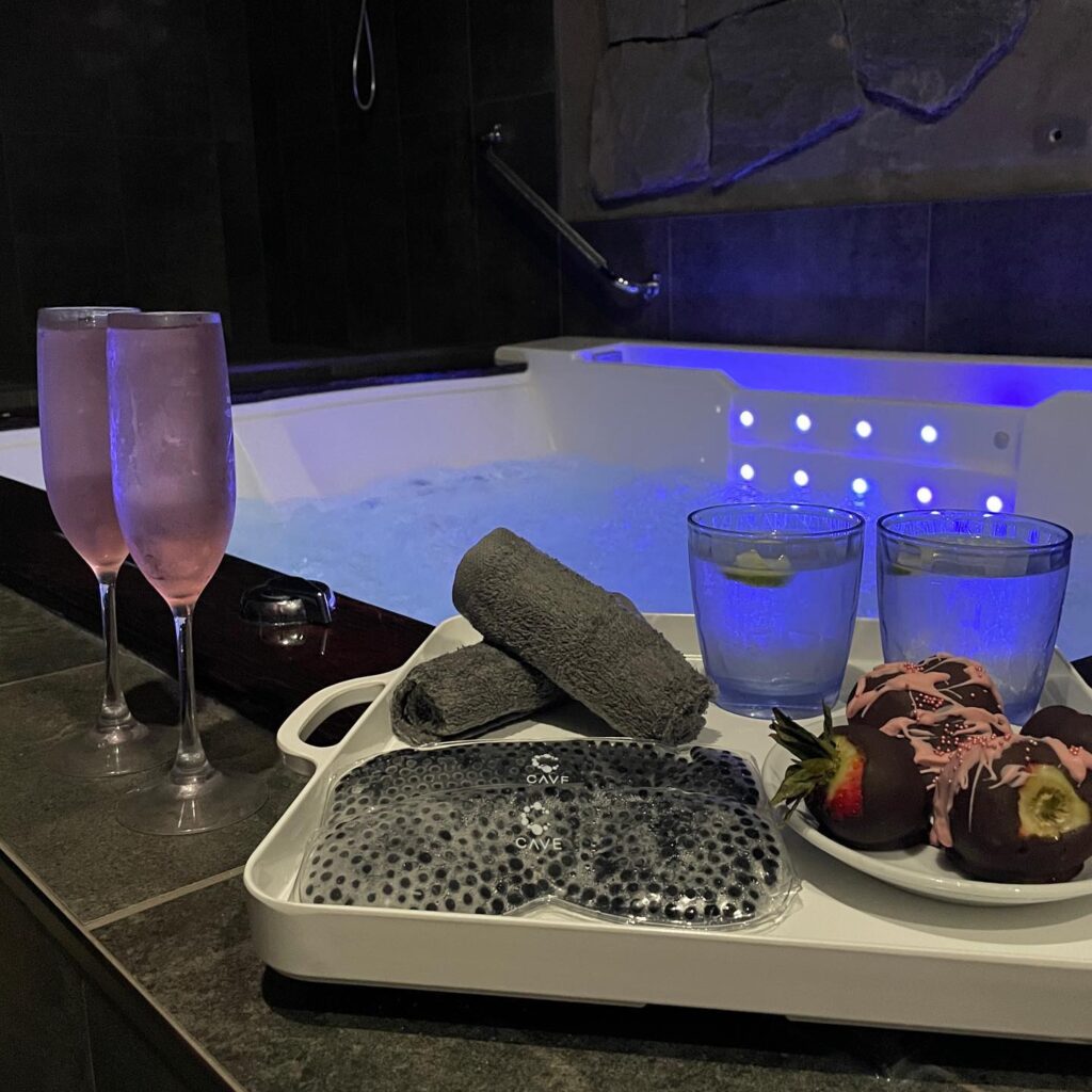 Champagne glasses, eye masks, and chocolate-covered strawberries sit next to a hot tub.