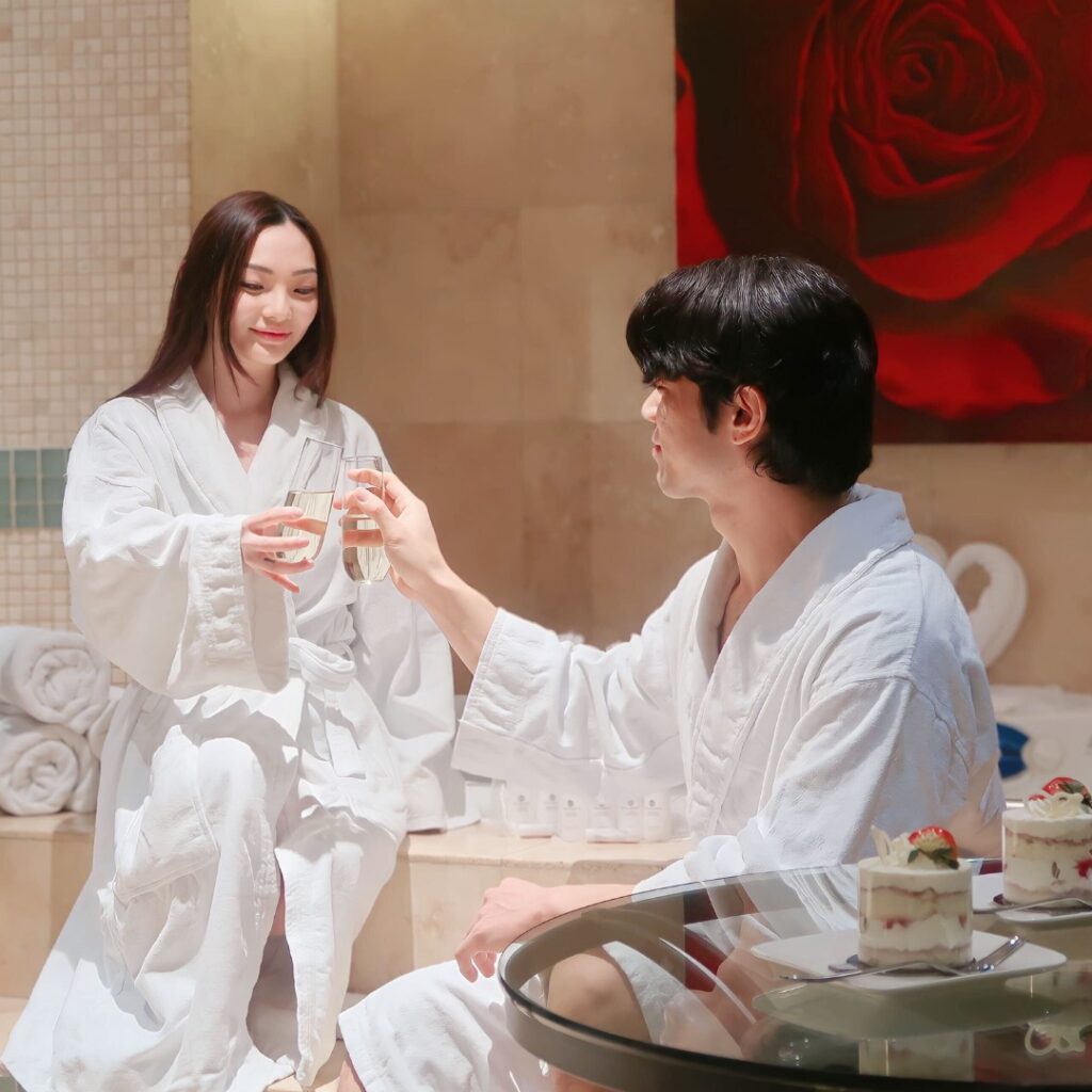 A couple clinks their glasses of champagne together while wearing bathrobes in a spa.