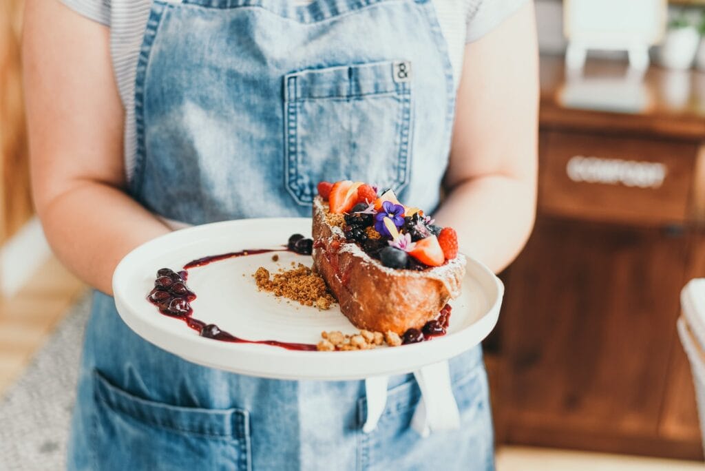 A person holds a plate of toast decorated with berries and flowers.