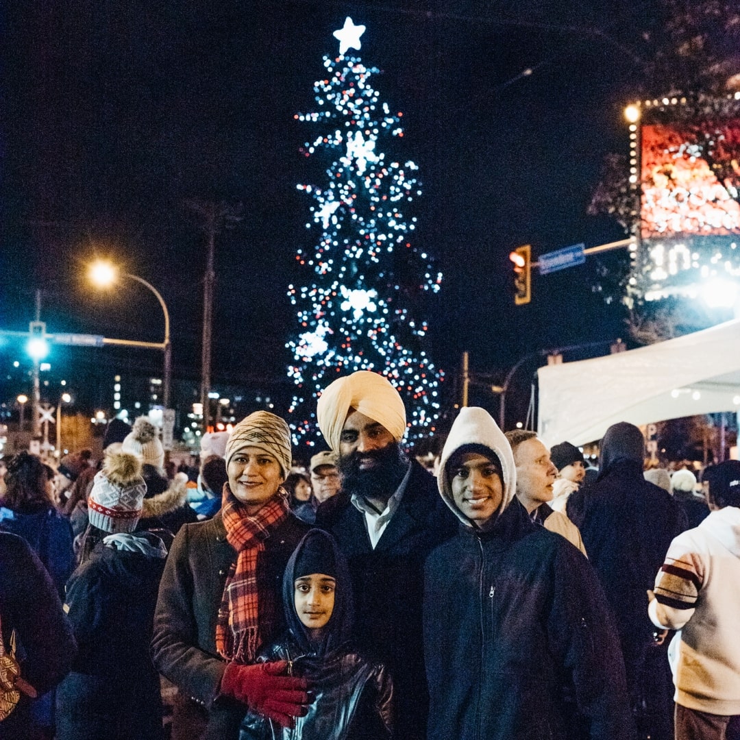 A group of people pose outside for a picture, with a brightly lit Christmas tree in the background