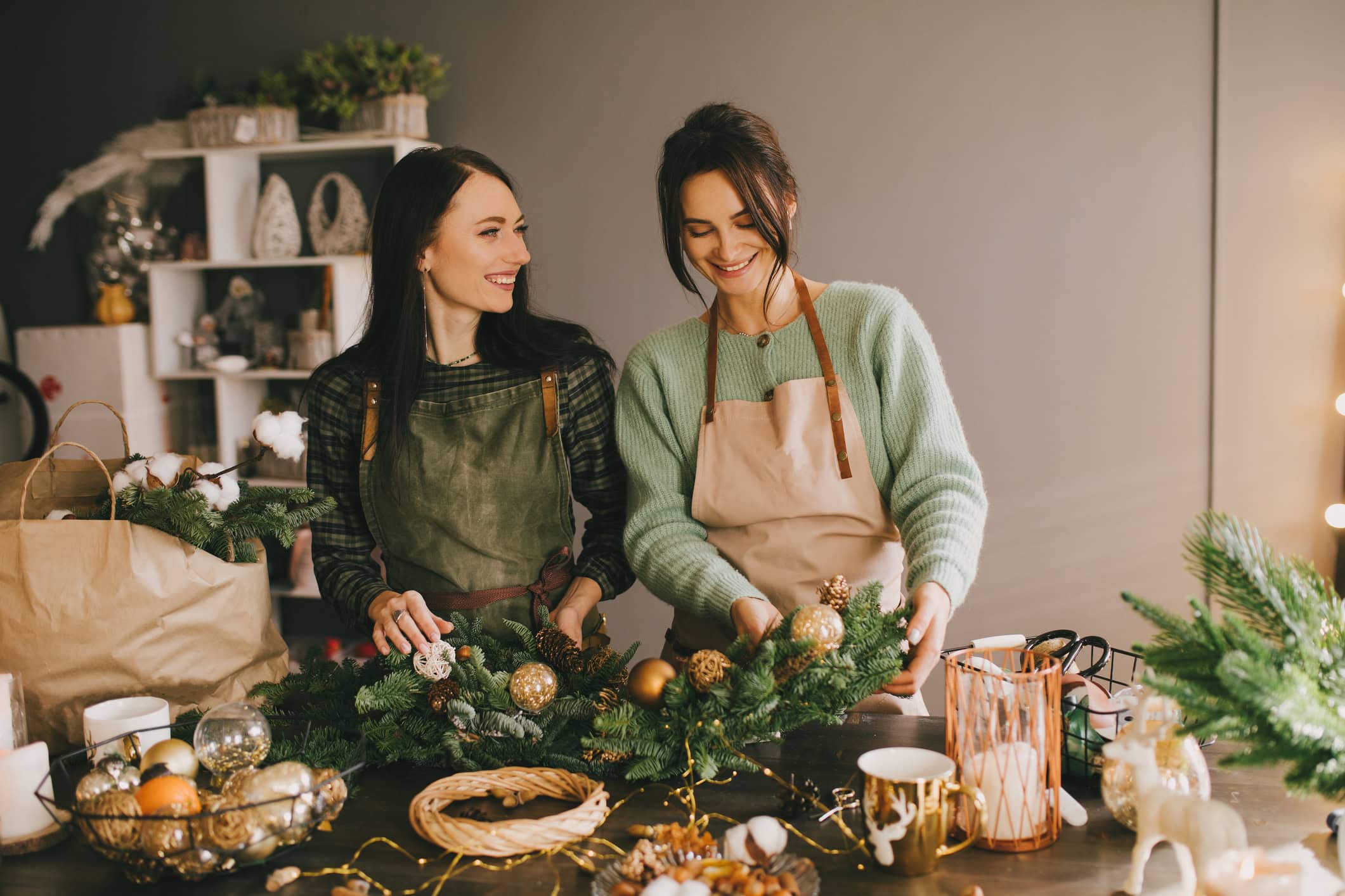 Two Millennial Women Making Christmas Wreath Using Pine Branches And Festive Decorations
