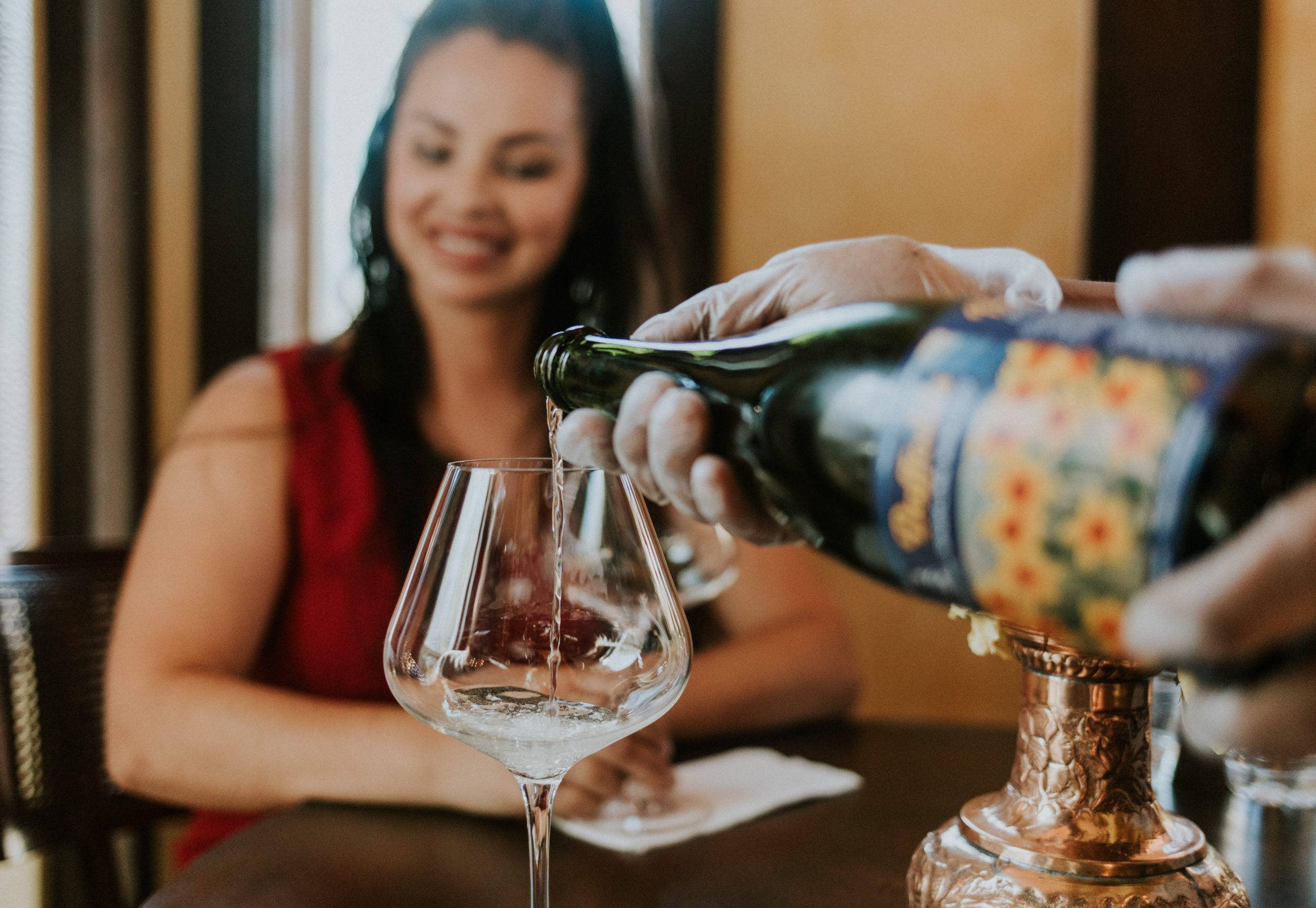 Wine being poured into a glass, while a woman looks on in the background