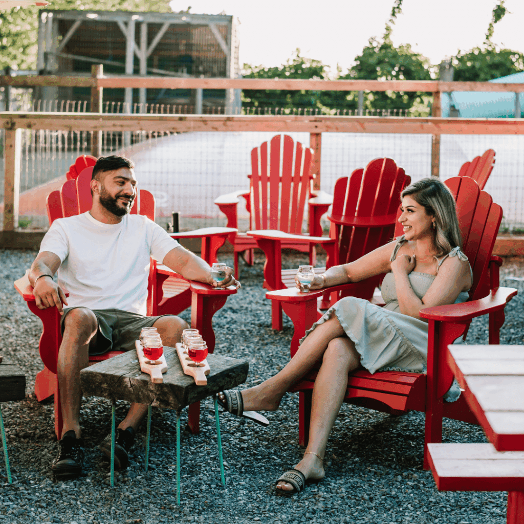 a couple sits on Adirondack chairs and sips ciders