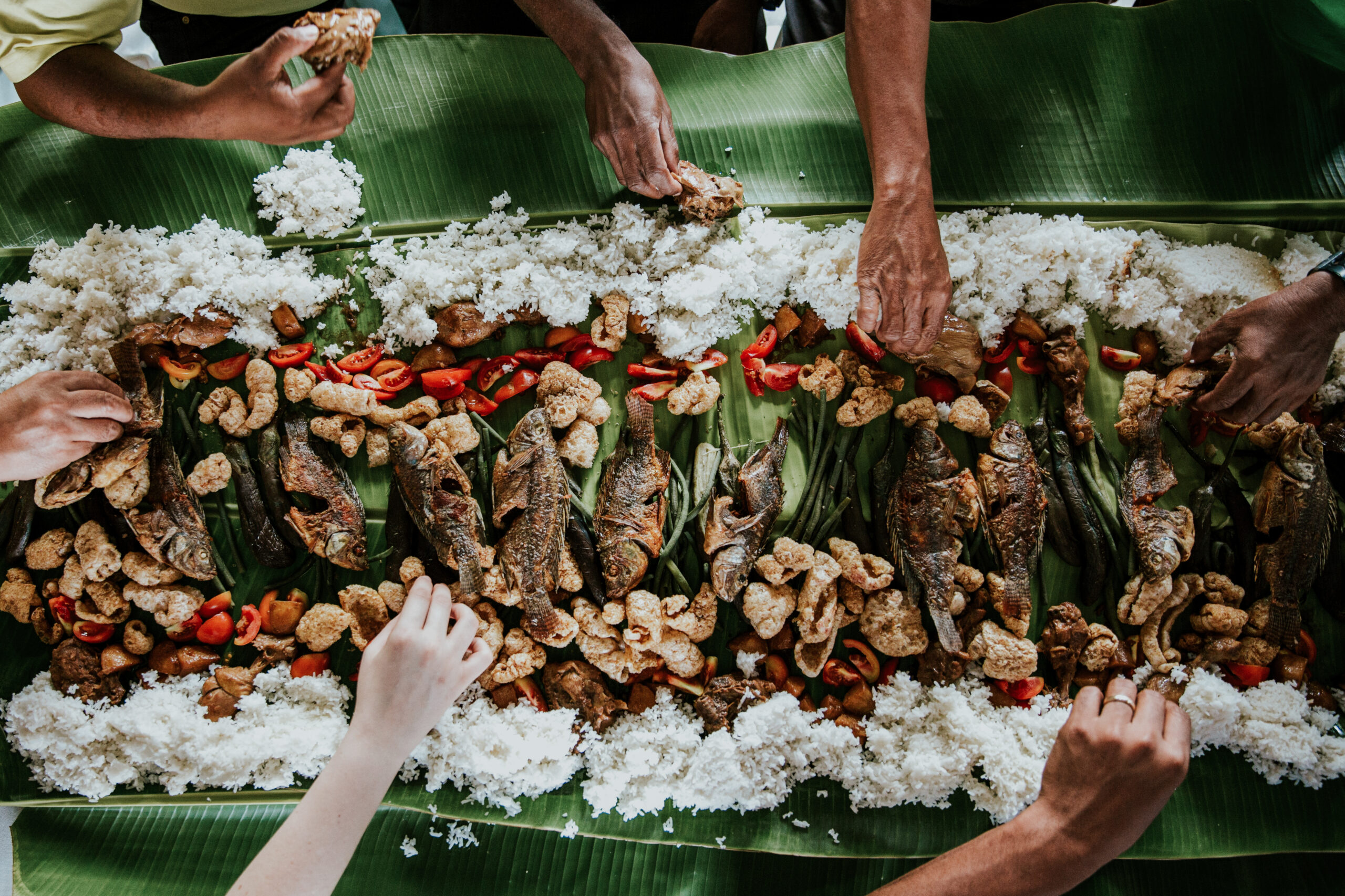 hands reaching for Filipino food laid out on banana leaves