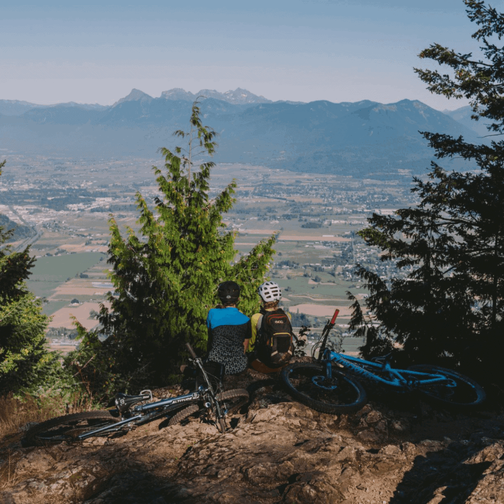 Two people on a mountain looking down at a valley, with their bikes laying behind them