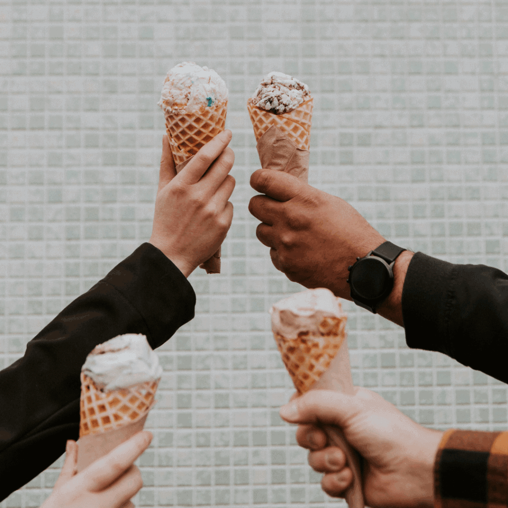 Hands holding ice cream cones in front of a blue tiled wall.