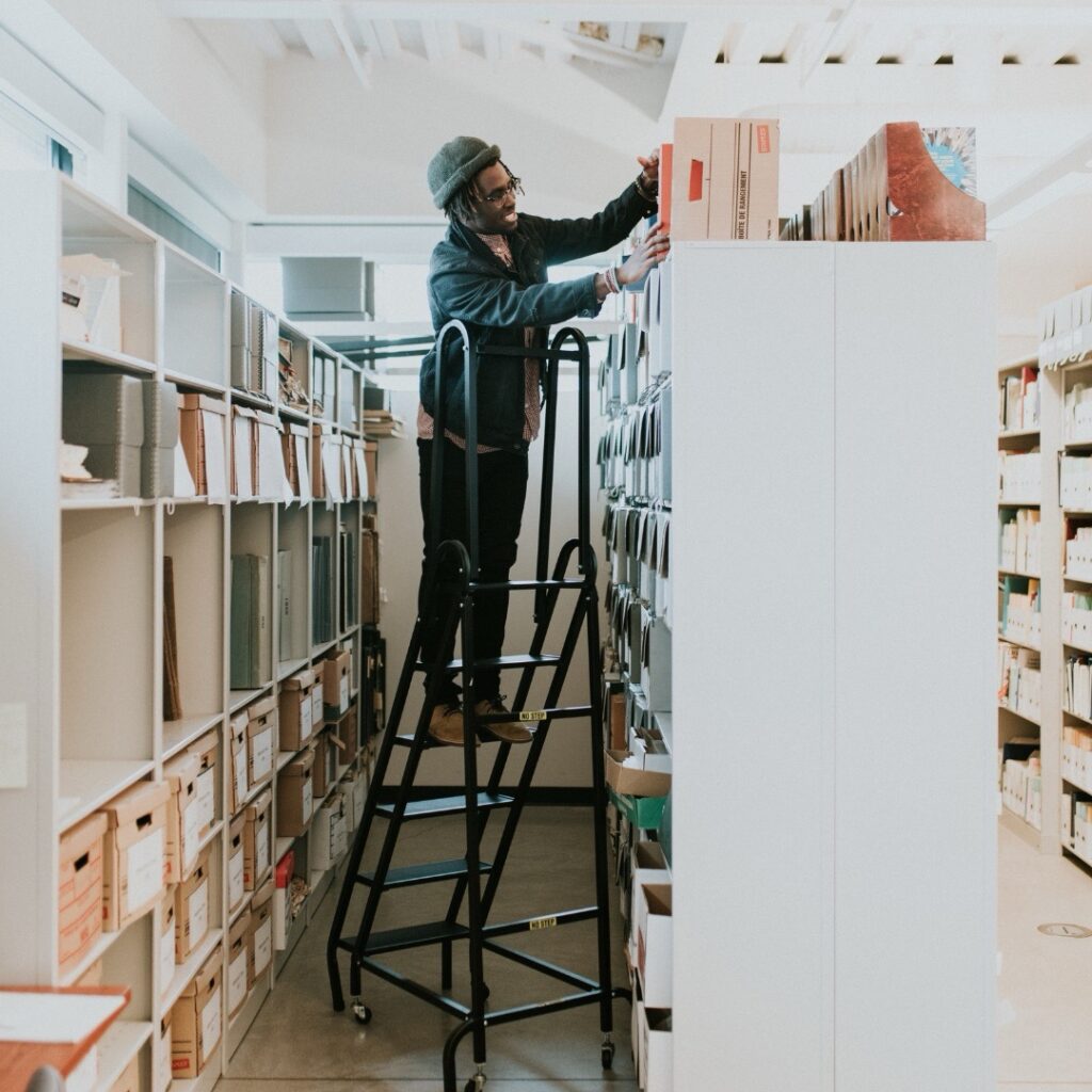 A man is standing on a ladder in a large warehouse.