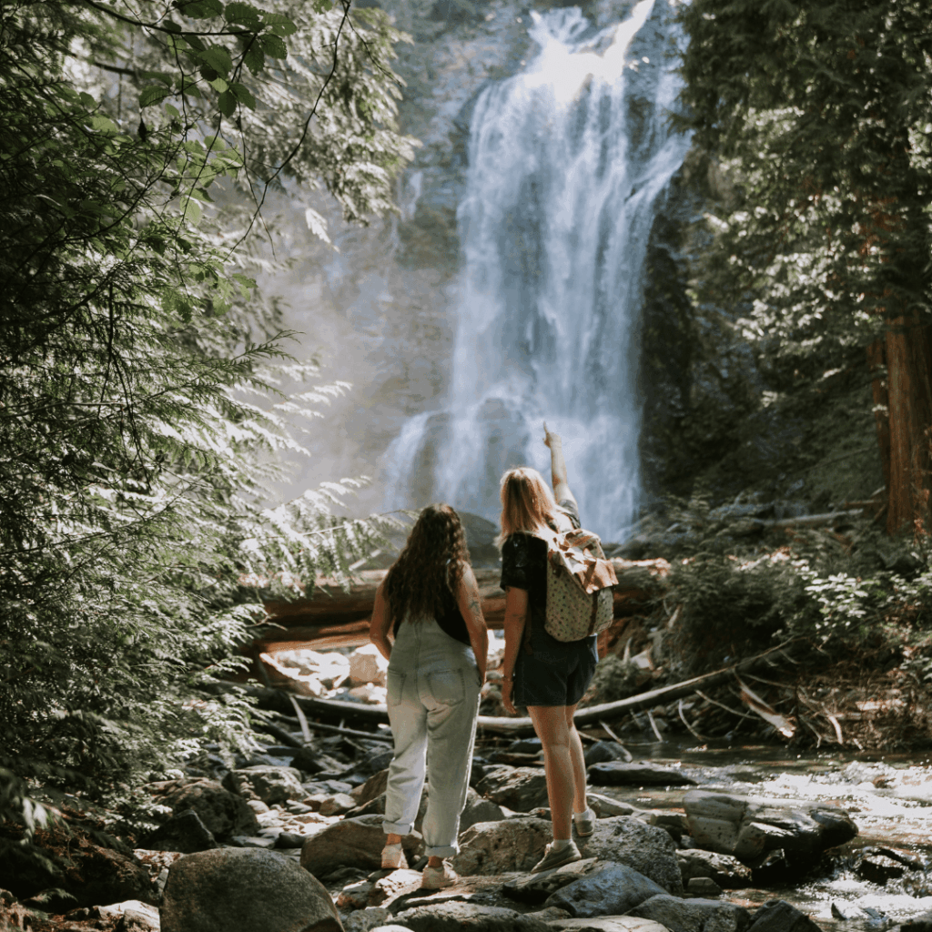 Two women walking in front of a waterfall.