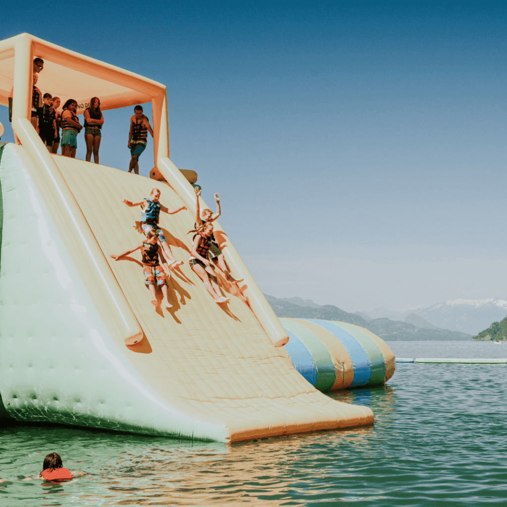 A large inflatable slide with kids sliding down into the lake