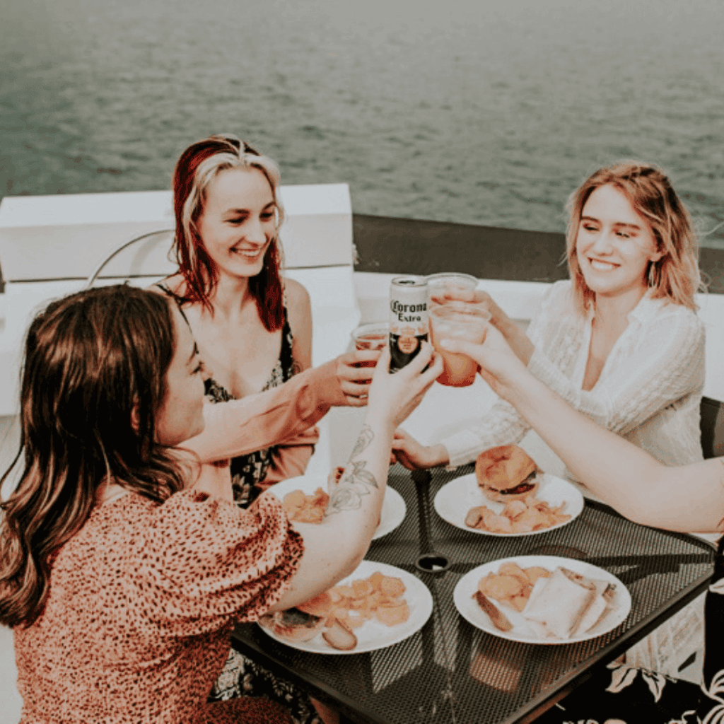 Four women toasting on a boat with food.