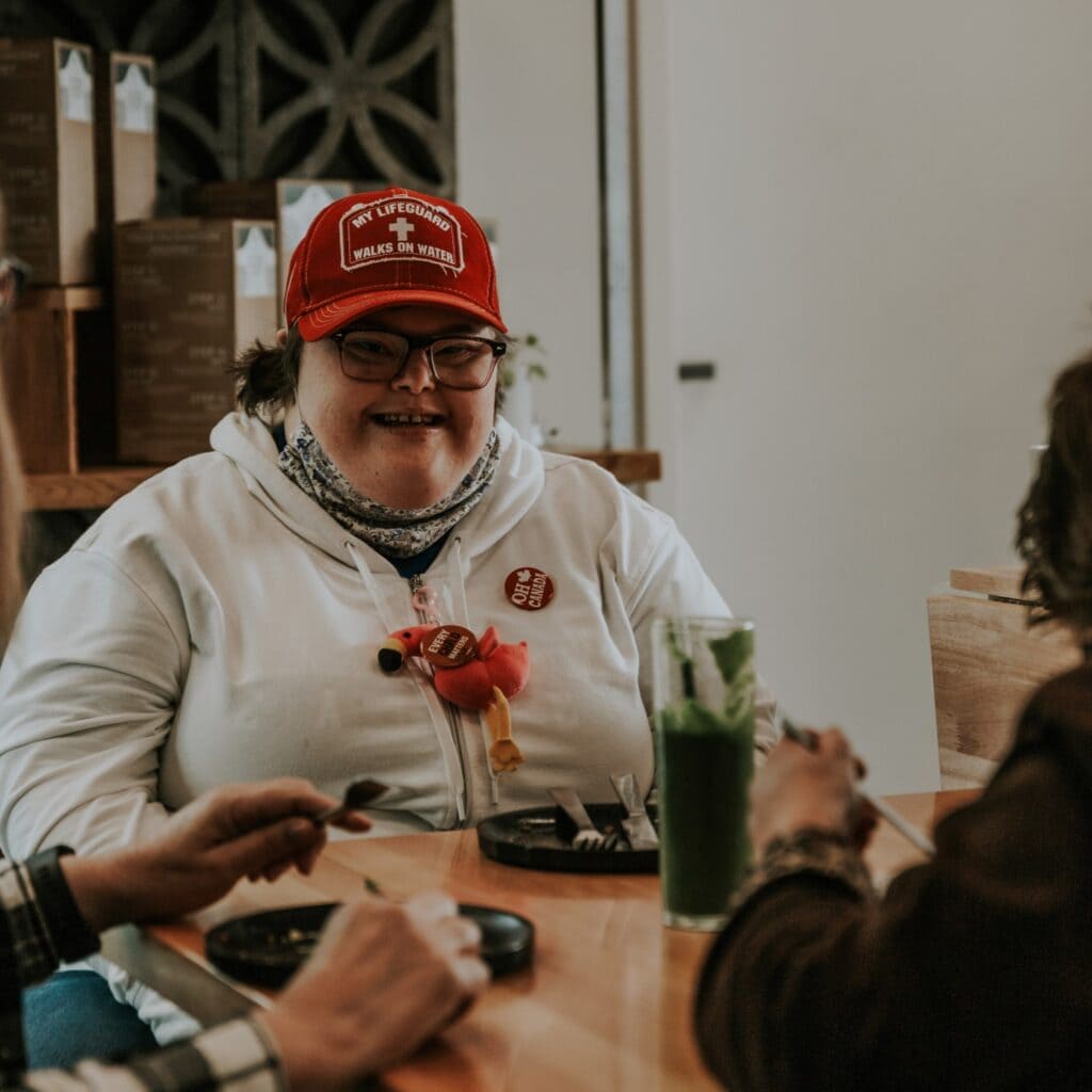 A woman wearing a red hat and a white shirt sitting at a table with food.