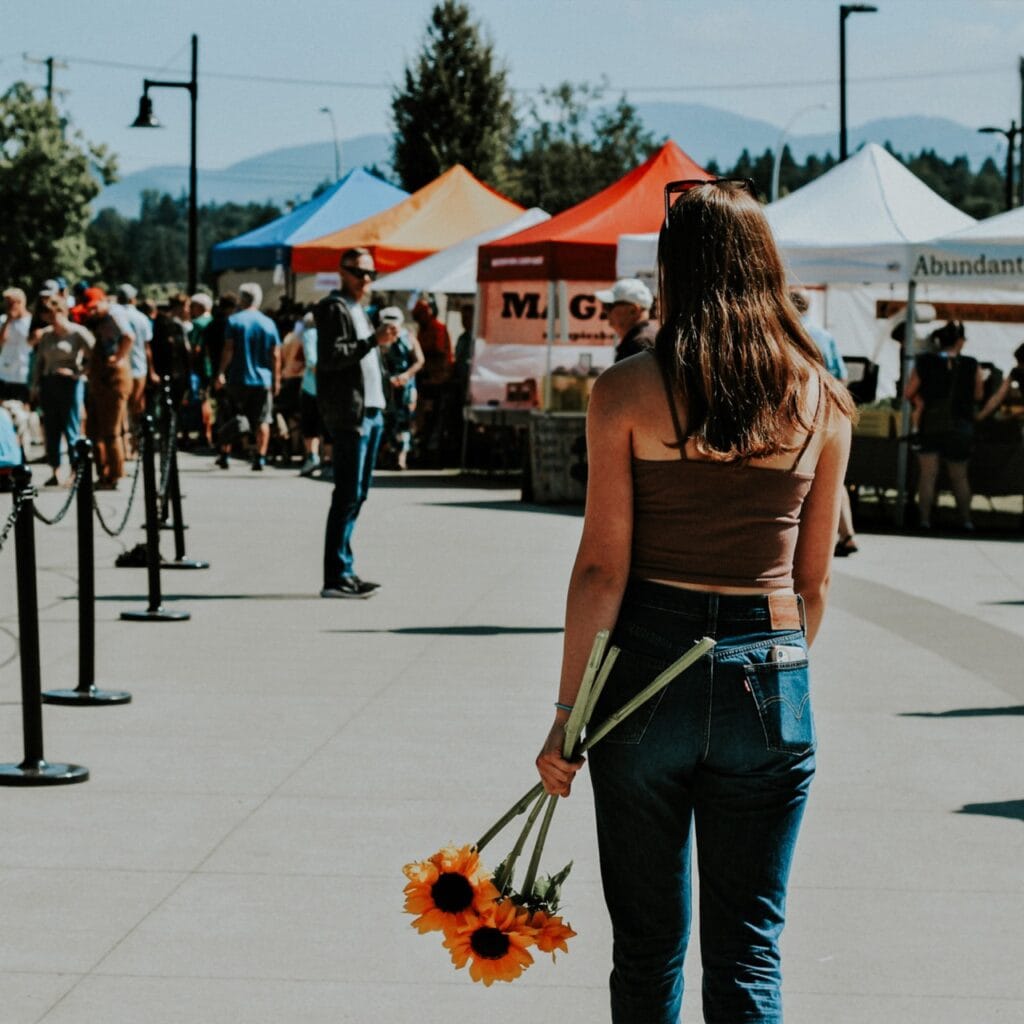 A woman walking down a sidewalk holding sunflowers.