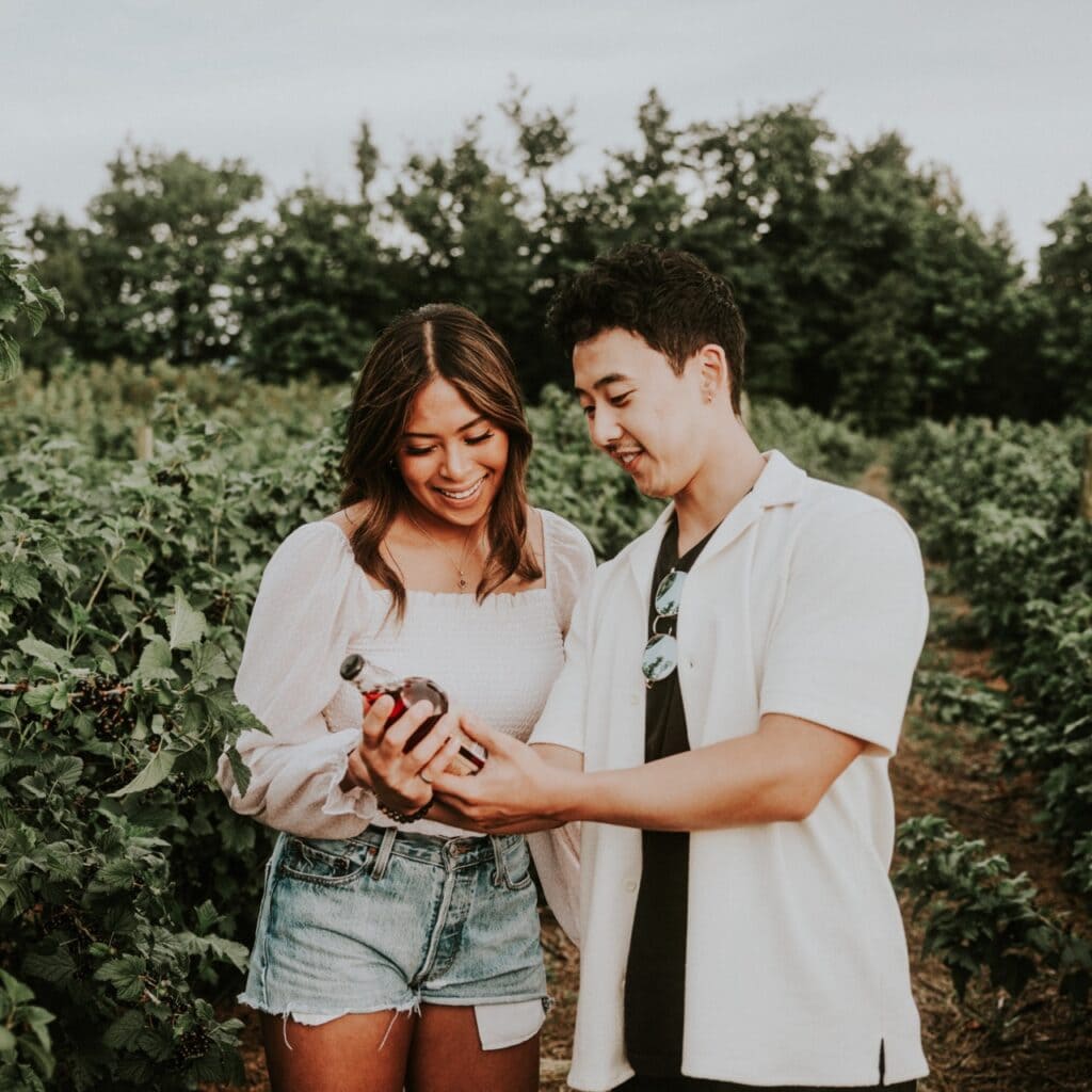 Two people in a field of fruit looking at a bottle