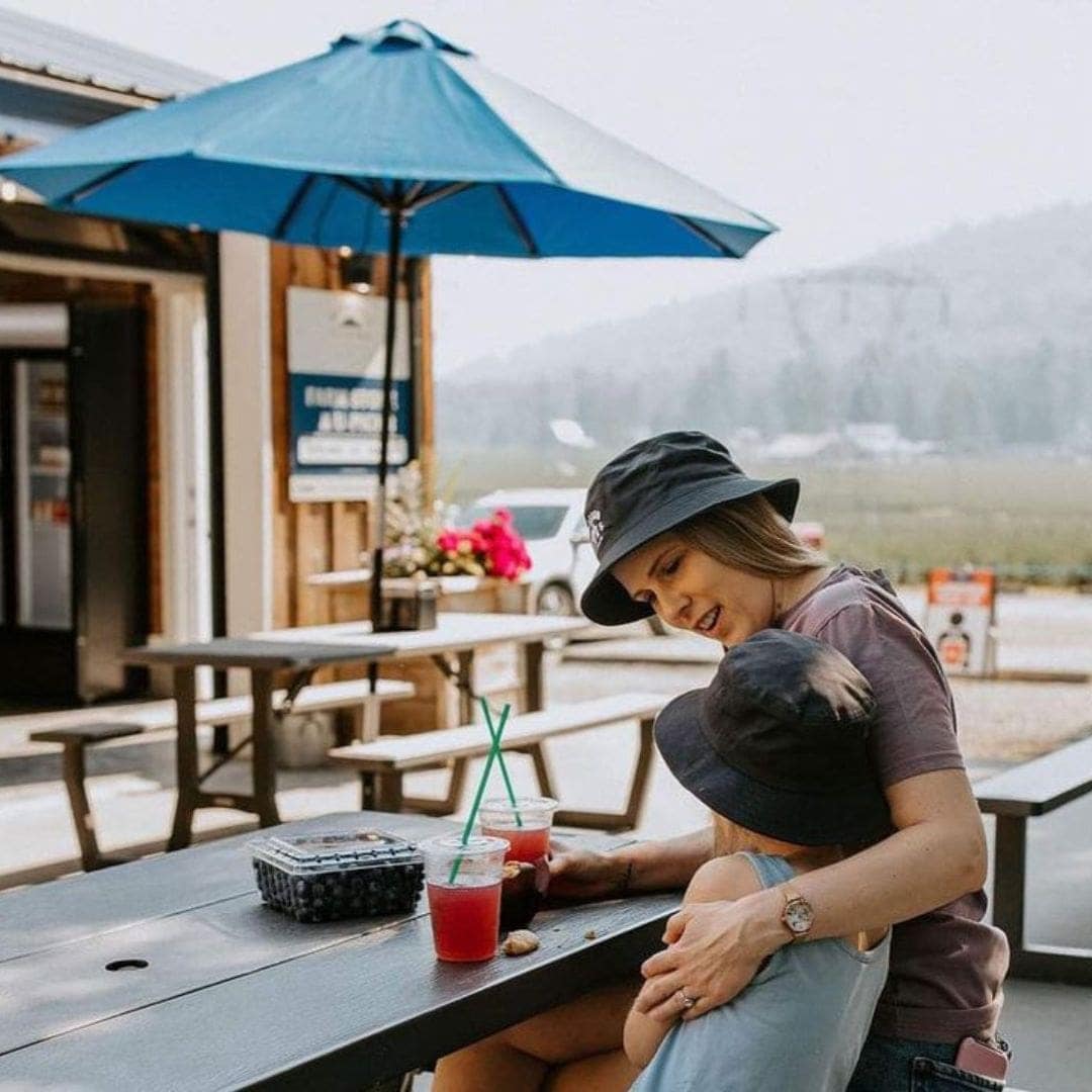 a woman and a young girl sit at a picnic table, enjoying a cold beverage