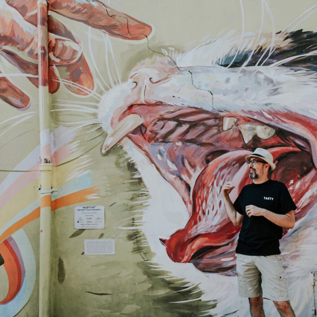 A man standing in front of a cat mural