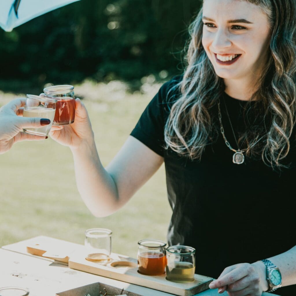 a woman smiles and clinks her glass of cider with someone else