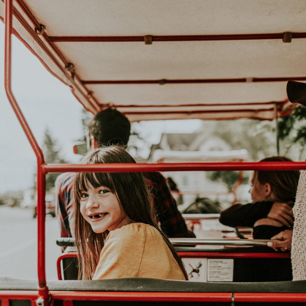 A small girl smiles at the camera from the back of a pedal bike