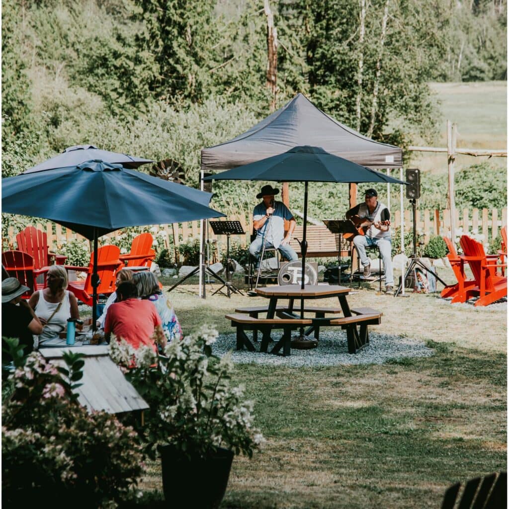 A group of people sitting at a picnic table, with a band in the background, playing music