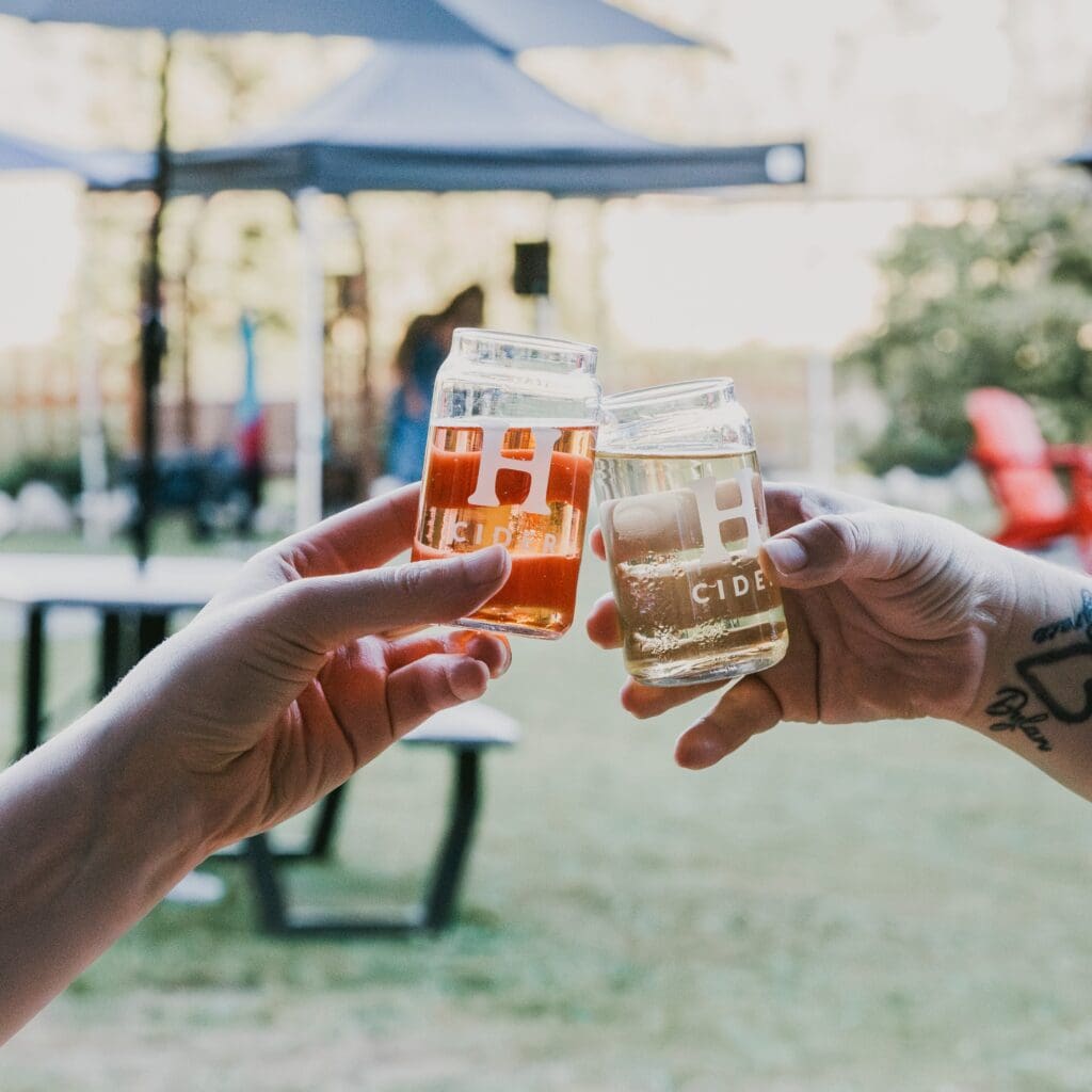 two hands holding glasses full of cider, clinking their glasses