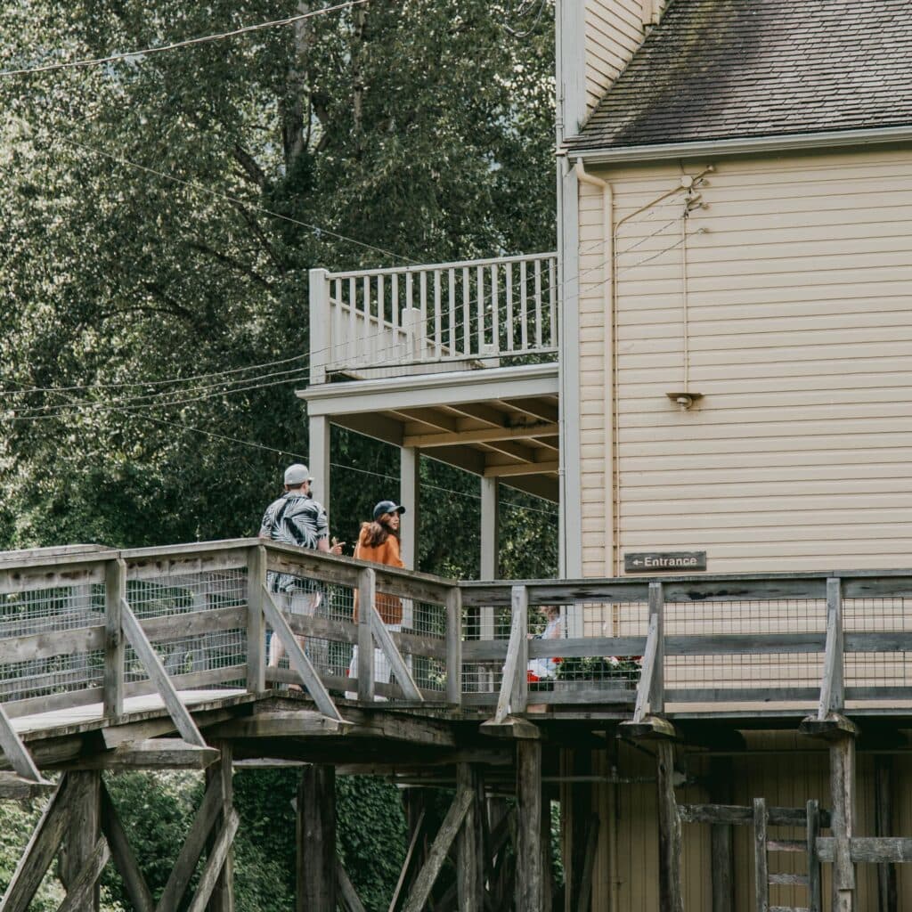 Two people walking on a wooden bridge towards a building