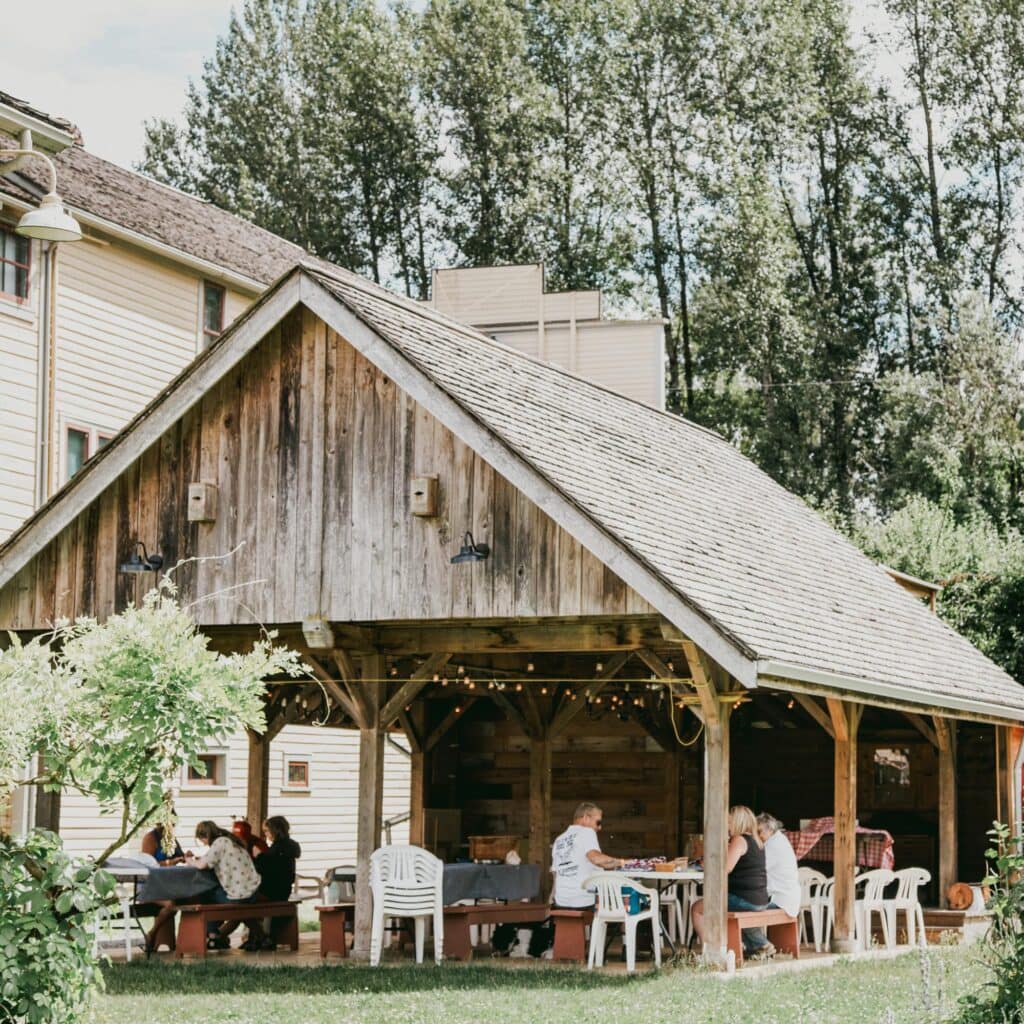 A rustic barn with tables and chairs in the yard.