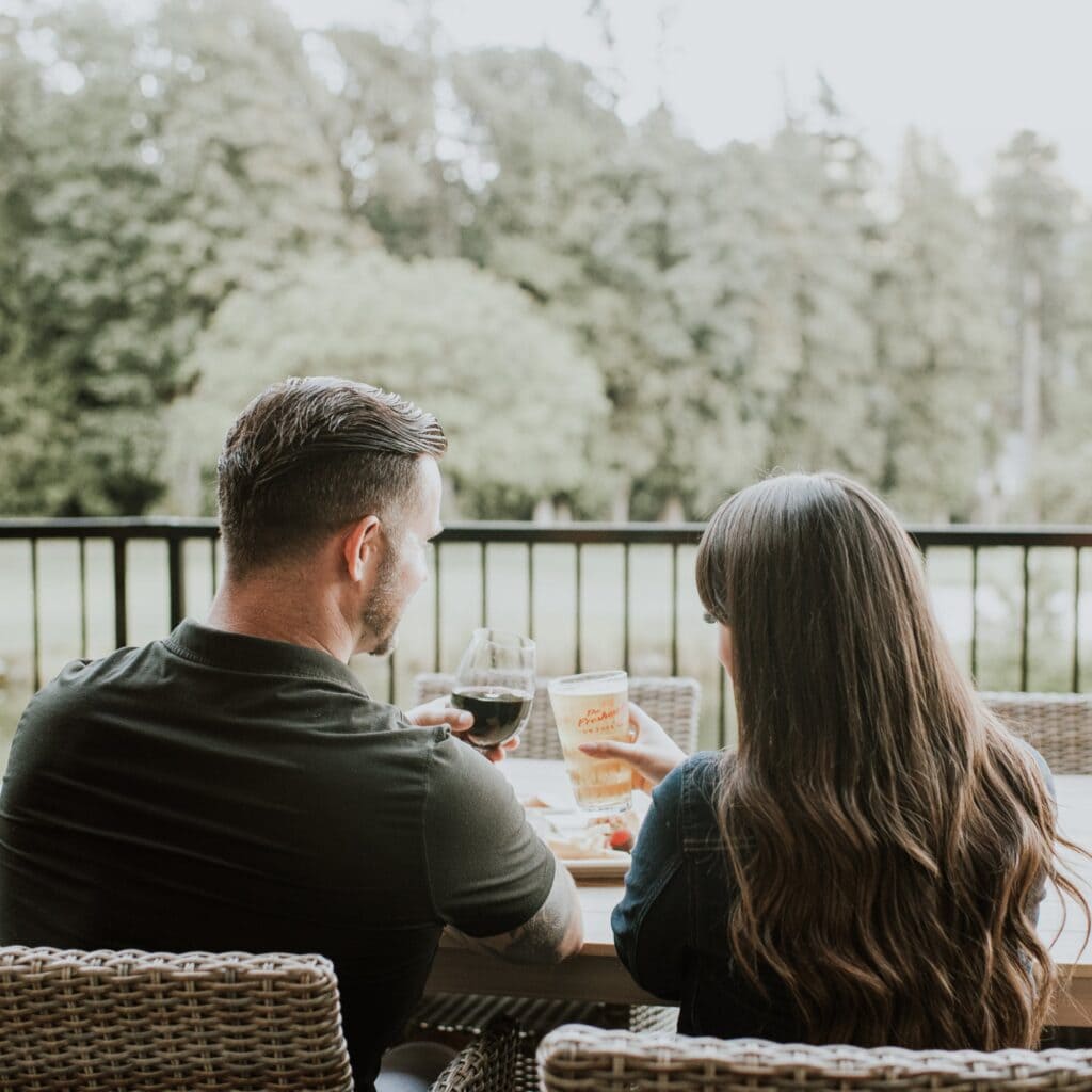Two people sitting on a patio, clinking their glasses 
