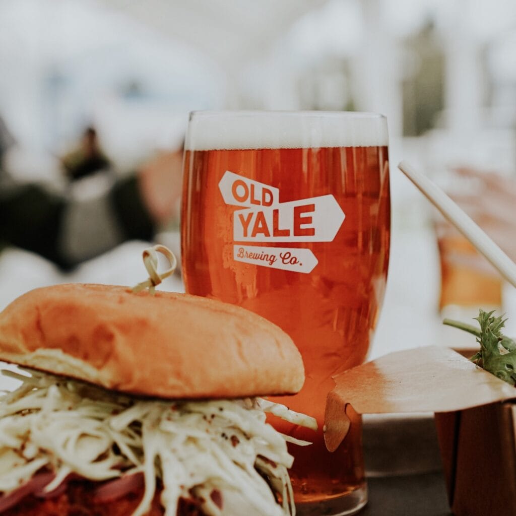 A sandwich and a cold beer in a glass that says "Old Yale Brewing"
