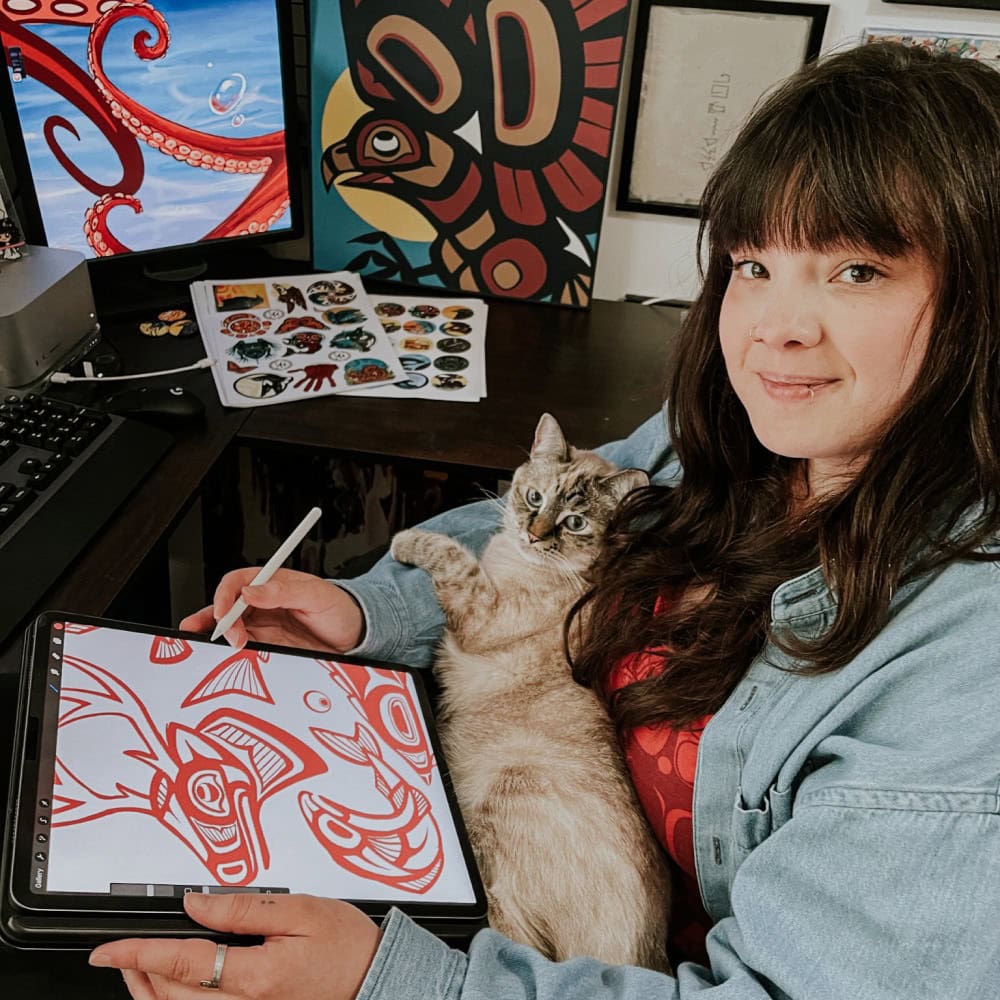 A woman holding a tablet with a cat sitting next to her.
