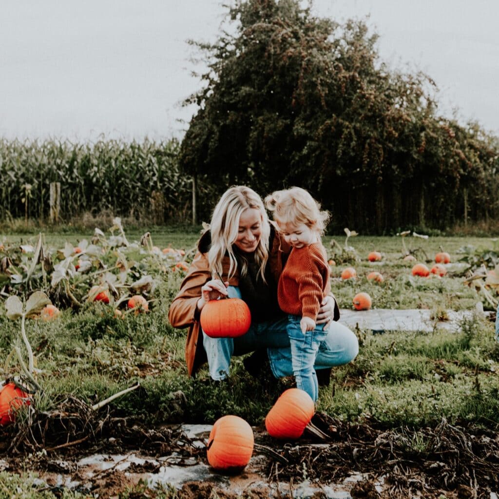 A mother and child pick a pumpkin in a patch