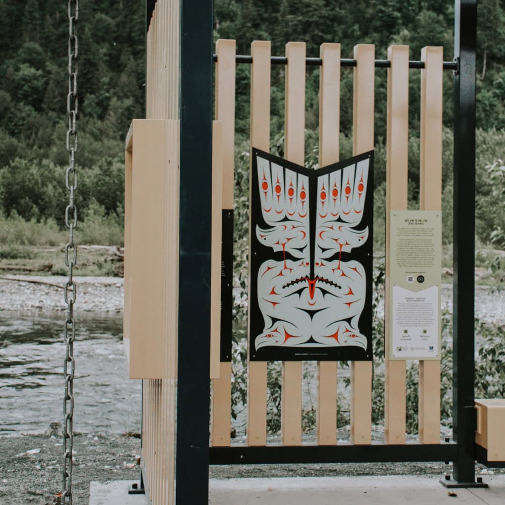 An indigenous art piece on a wooden slat, with a river in the back
