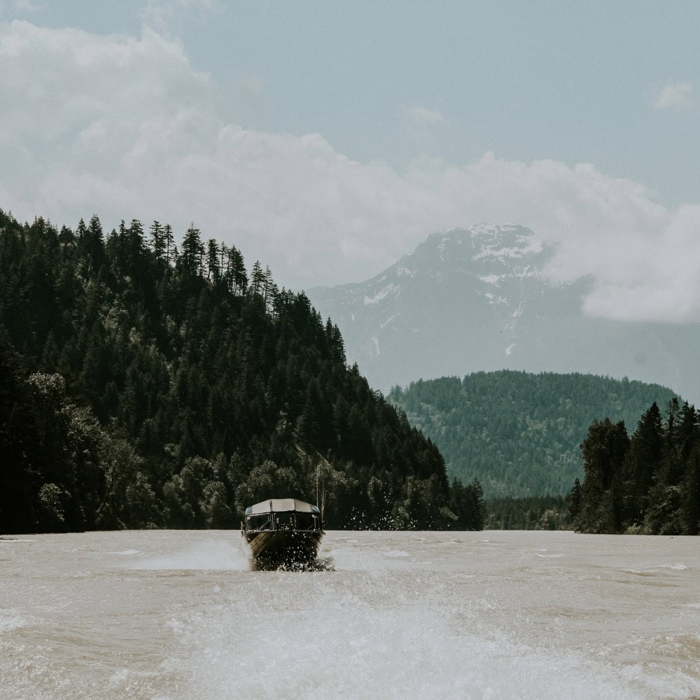 A boat rides along a river, with surrounding green mountains