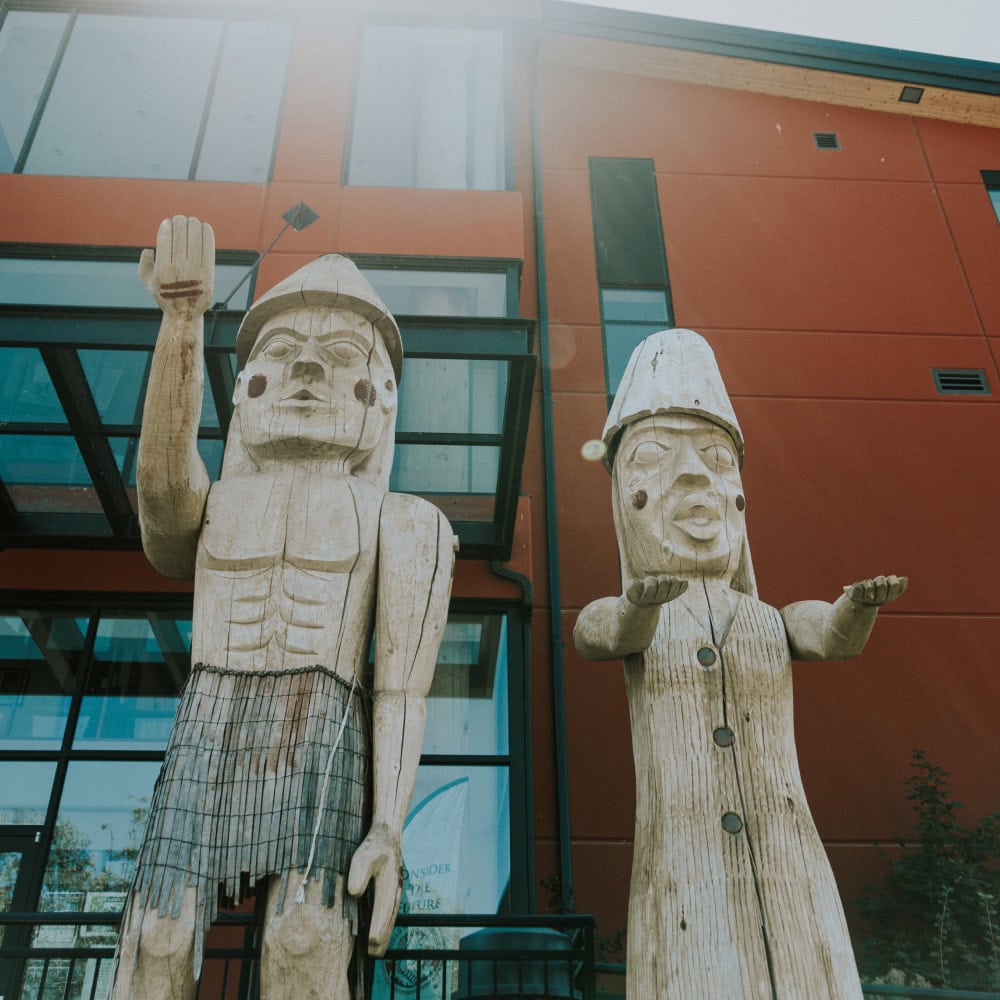 Two large indigenous carvings in front of a building