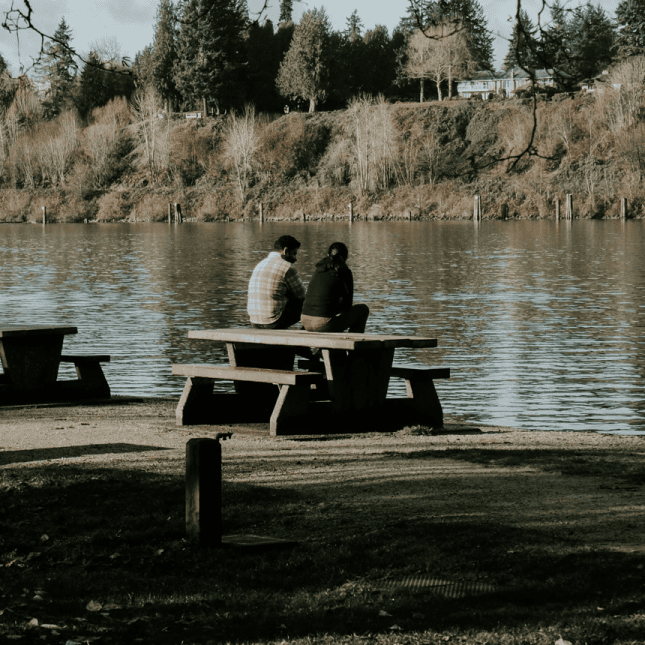 Two people sitting on a bench with river in the back